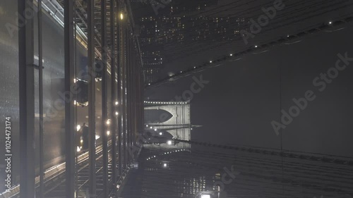 Vertical video of cars passing on the Brooklyn Bridge in New York, USA, filmed on a dark, cold, and foggy night, with the city's skyscrapers in the background.