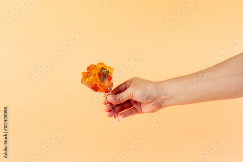 Fruit flavored worm shape, jelly candies in a glass and woman's hand on cream background.