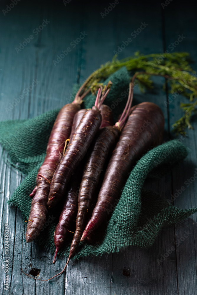 A bunch of purple carrots are on a green cloth. The carrots are long and slender