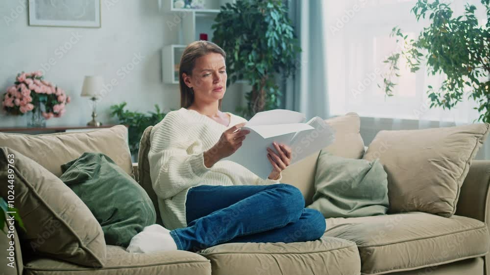 Woman sits comfortably on a couch, reading a book. After putting the book down, she leans back, becoming lost in thought and enjoying a moment of peaceful reflection Woman sits comfortably on a couch, reading a book. After putting the book down, she leans back, becoming lost in thought and enjoying a moment of peaceful reflection