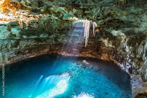 Man swimming in the blue water of a cenote with sunlight from the top, Yucatan, Mexico