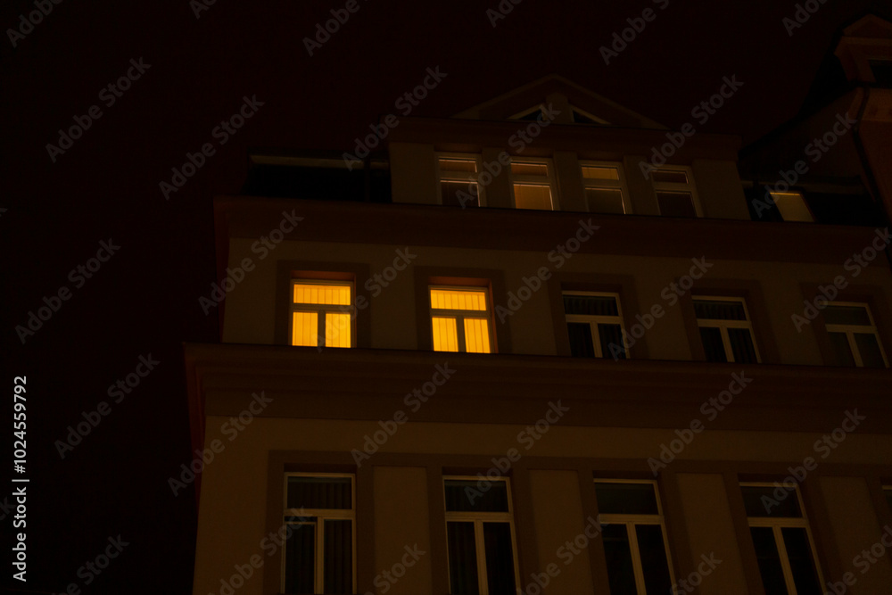 At night, the windows of a building are illuminated, casting light into the surrounding space and creating a warm atmosphere At night, the windows of a building are illuminated, casting light into the surrounding space and creating a warm atmosphere