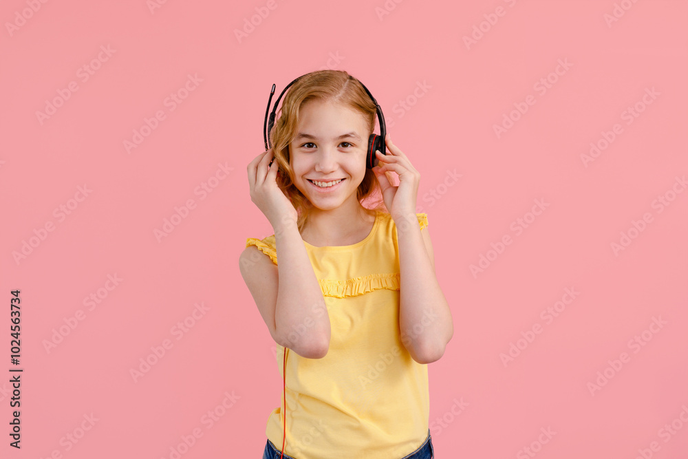 Blonde girl wearing headphones looking at her phone against pink background Blonde girl wearing headphones looking at her phone against pink background