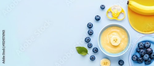 Colorful baby food scene with banana, blueberries, and bib on a light blue background.