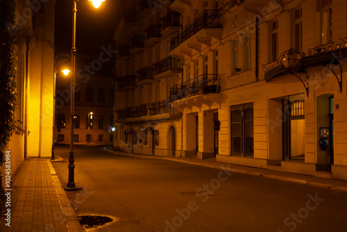 Fotografi An empty street during the night hours, with tall buildings lining both sides an