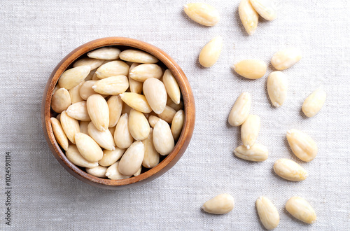 Freshly blanched almonds in a wooden bowl on linen. Shelled almonds that have been treated with hot water to soften the seed coat, which is then removed to reveal the seed. Fruits of Prunus amygdalus.