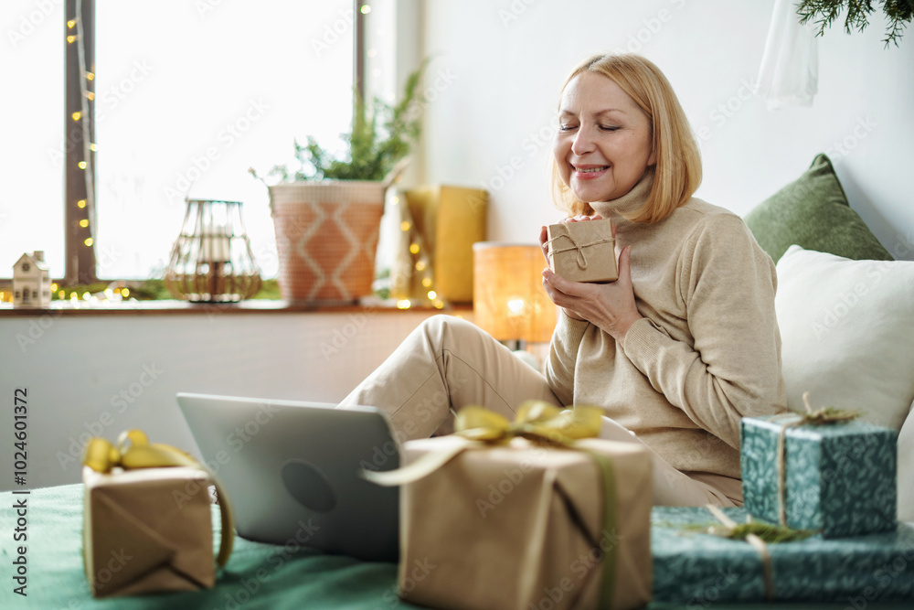 Mature woman sitting on sofa with Christmas presents doing a video call. Unpacking parcels with gifts, season of giving. Christmas time, Mature woman sitting on sofa with Christmas presents doing a video call. Unpacking parcels with gifts, season of giving. Christmas time,
