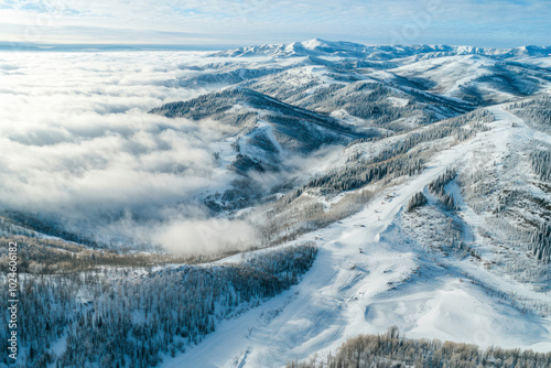 Aerial view of the stunning winter panorama of the snowy slopes and hills among the lush white clouds.