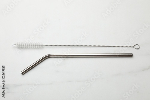 Metal drinking straw and cleaning brush on light marble table, flat lay