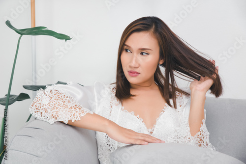 A woman uses her hand to comb through her tangled hair while sitting on a couch.