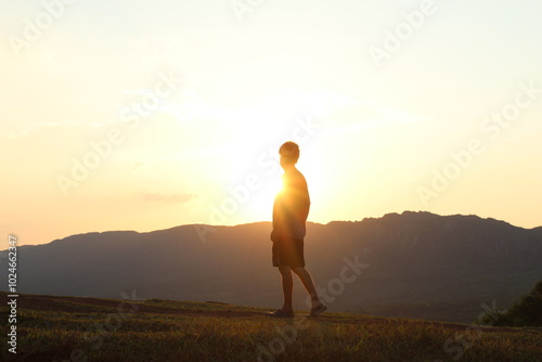 silhueta de homem caminhando com sol ao fundo e montanhas 