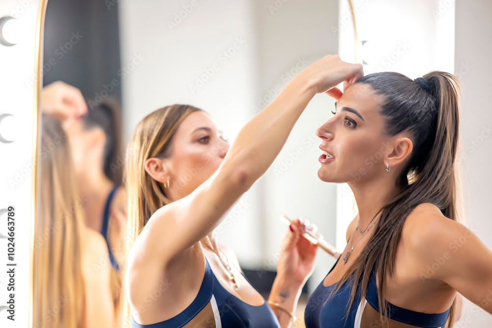 A woman gently fixing her partner's hair during makeup application, both wearing navy sportswear, indoors. A woman gently fixing her partner's hair during makeup application, both wearing navy sportswear, indoors.
