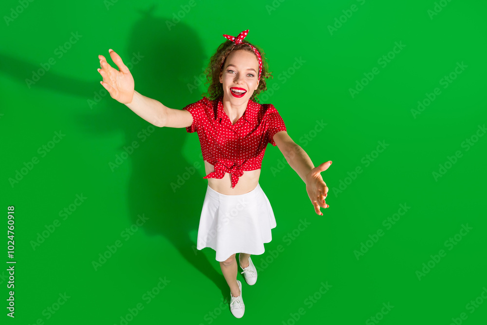 Full size photo of pretty young girl tow view stretch hands wear trendy red retro outfit isolated on green color background Full size photo of pretty young girl tow view stretch hands wear trendy red retro outfit isolated on green color background