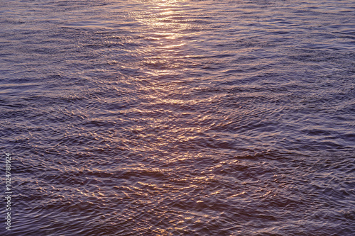 Wavy water texture with ripples and sun glare at sunset.