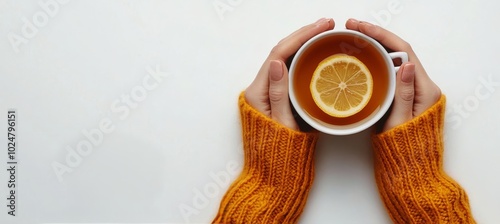 Warm hands holding a cozy cup of lemon tea on a neutral background during a c...