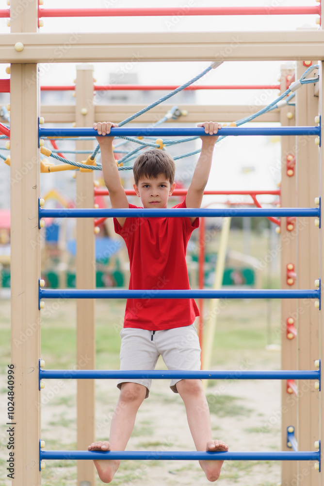 Obraz premium Happy boy playing and hanging on steel bar on playground. Children's exercises for health and concentration.