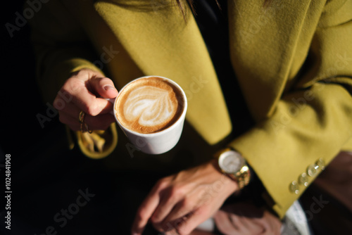 close-up hands holding a cup of coffee against the background of a street cafe with space for an inscription