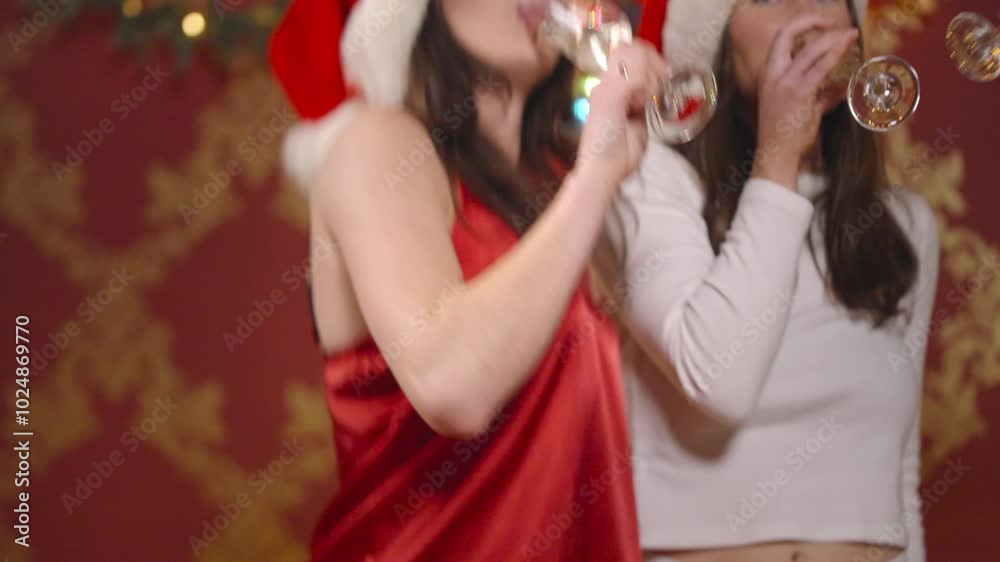 Women in pajamas and Christmas hats cheers with champagne in front of a holiday backdrop