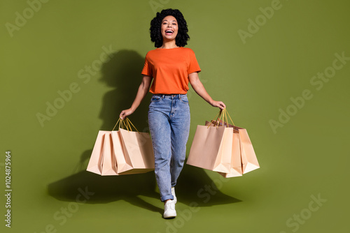 Full size photo of pretty young woman walk hold bags wear t-shirt isolated on khaki color background