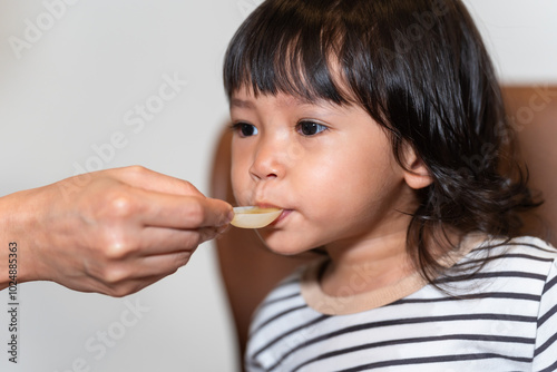 mother feeding liquid medicine to sick toddler baby with spoon photo