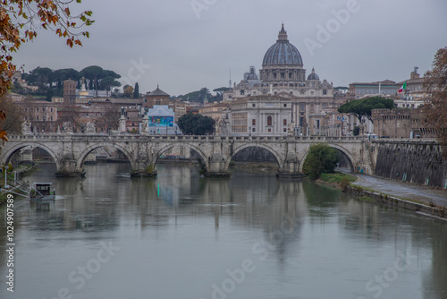 View over the Tiber River in a historic city. The old well-known bridge Ponte Sant'Angelo, in the evening. Rainy weather at sunset and view of the Basilica di San Pietro, Rome, Italy