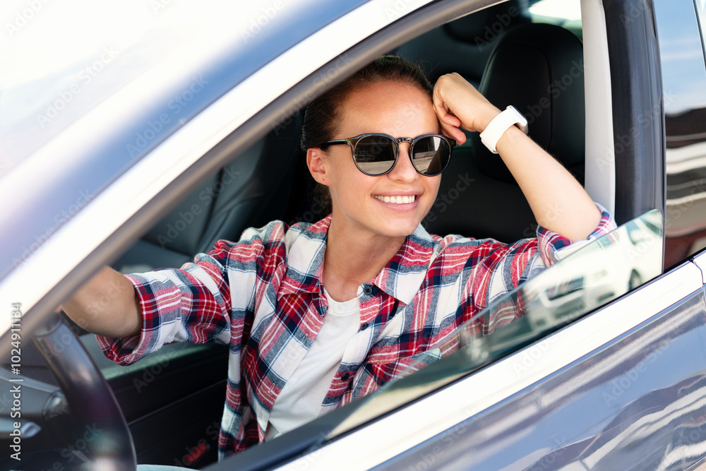 Naklejka premium Cheerful young woman sits in her car and smiling. Road trip vacation. Mobility service. Car rental.