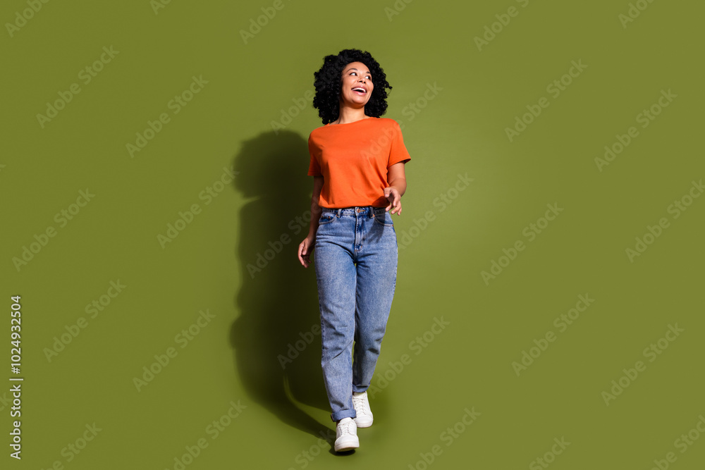 Full size photo of pretty young girl walking look empty space wear trendy orange outfit isolated on khaki color background Full size photo of pretty young girl walking look empty space wear trendy orange outfit isolated on khaki color background