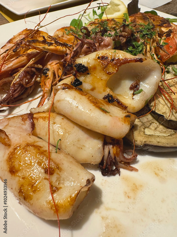 Grilled seafood platter with squid, shrimp, and herbs on a white plate Grilled seafood platter with squid, shrimp, and herbs on a white plate
