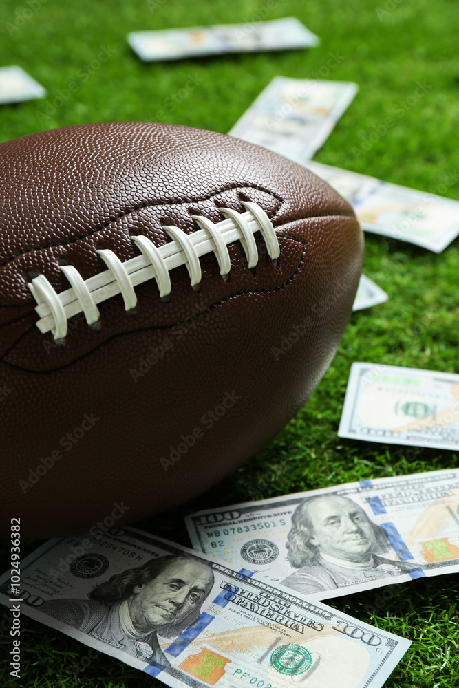 Obraz premium American football ball and dollar banknotes on green grass outdoors, closeup