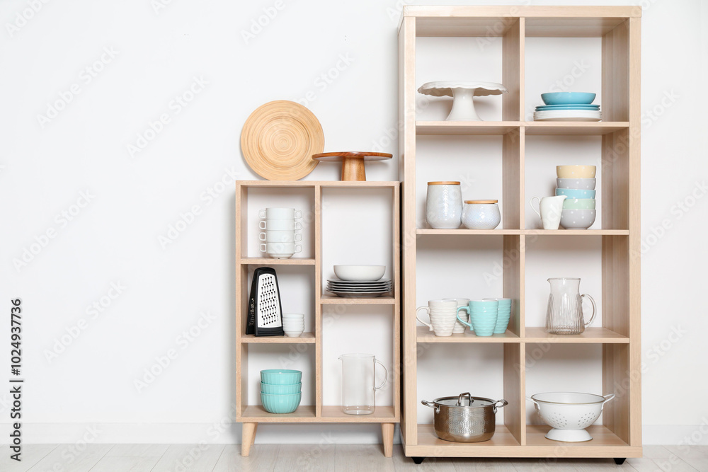 Wooden shelving units with kitchenware near white wall indoors Wooden shelving units with kitchenware near white wall indoors