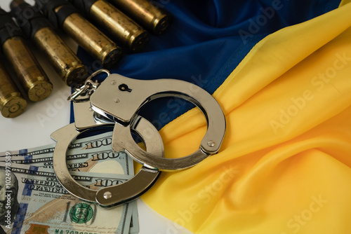 the concept of corruption when buying weapons. Handcuffs, American dollars and cartridges on the background of the yellow blue flag of Ukraine