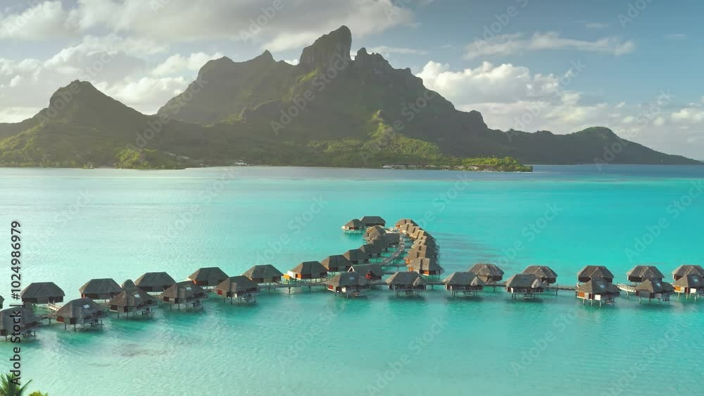 Aerial view overwater bungalows forming line towards mount Otemanu on tropical exotic Bora Bora island, with its turquoise lagoon and lush vegetation. Luxury travel vacation resort in coral reef ocean