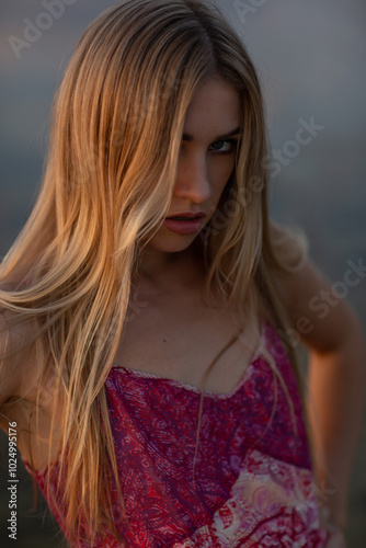 Fotografie A beautiful young woman in a pink dress is sitting in the water on the seashore at sunset