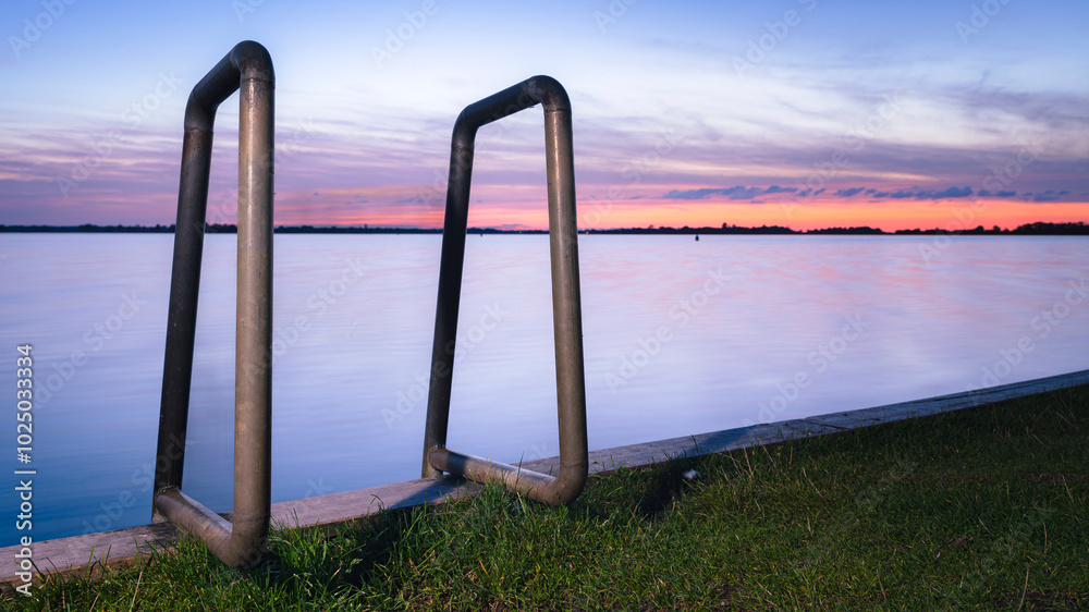 Metal brackets of a swimming ladder and sunshine through clouds. wooden quay at a lakeside. Metal brackets of a swimming ladder and sunshine through clouds. wooden quay at a lakeside.