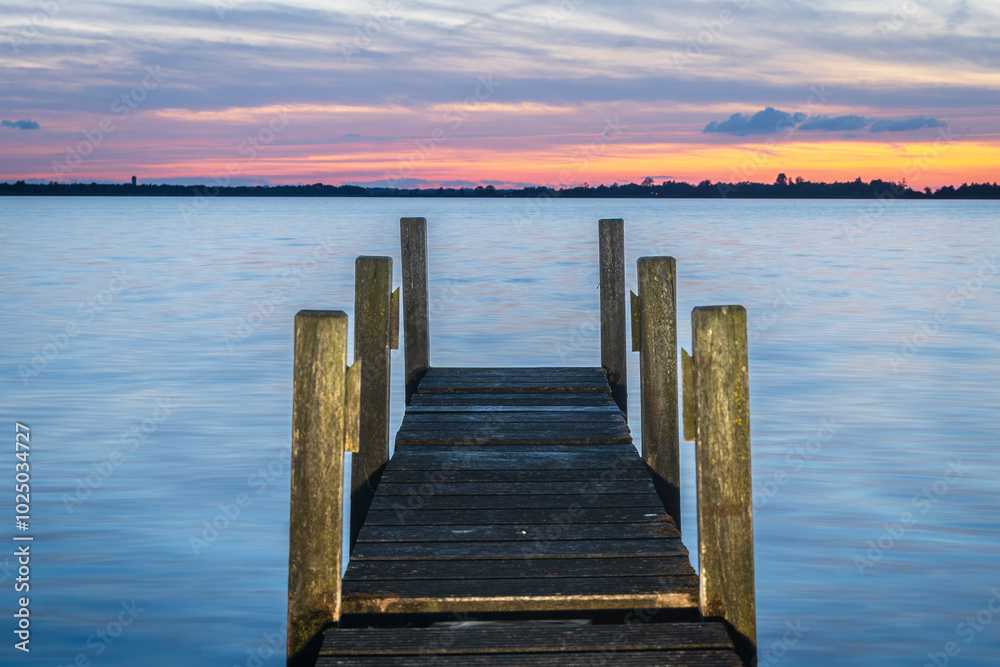 Fototapeta premium Beautiful blue and orange sunset with wooden dilapidated Jetty stretching out over the water surface