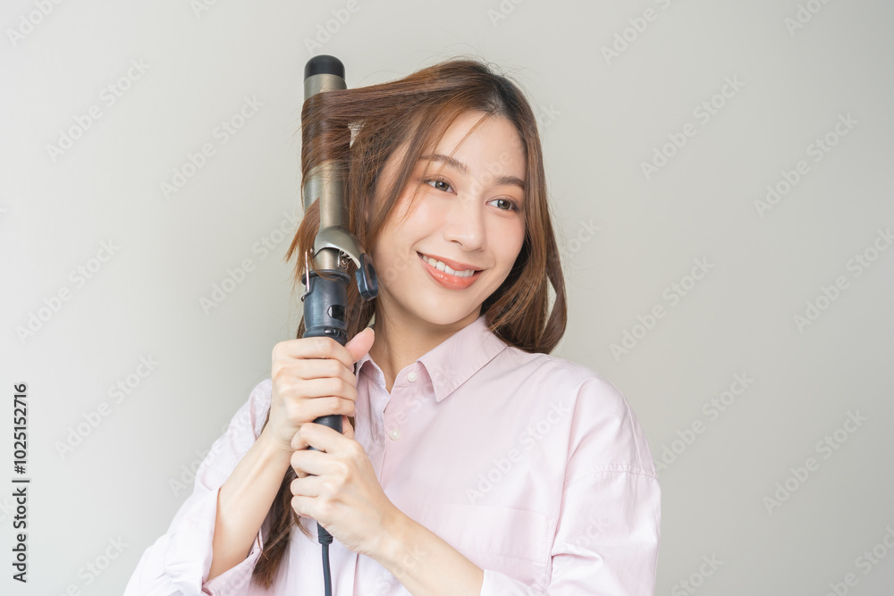 Beautiful curly brunette, attractive asian young woman, girl smiling using curler, curling iron long hair with ceramic curler straightener at home. Hairstyle and Hairdressing. Beauty and hair care. Beautiful curly brunette, attractive asian young woman, girl smiling using curler, curling iron long hair with ceramic curler straightener at home. Hairstyle and Hairdressing. Beauty and hair care.