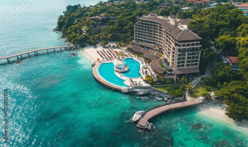 Aerial view of luxury hotel and beach with ocean view, pool, chairs, and bridge
