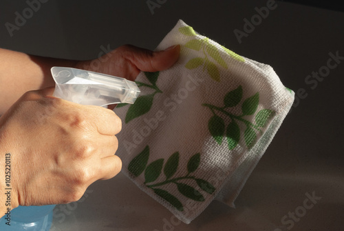 A woman's hand wiping the surface of the table in the kitchen with a rag and detergent spray. Cleaning concept