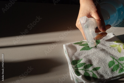 A woman's hand wiping the surface of the table in the kitchen with a rag and detergent spray. Cleaning concept
