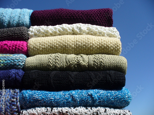 Hand-made warm sweaters and vests from various types of yarns evenly arranged - composition with blue sky. Topics: warm clothes, tidiness, fashion, hobby, handicraft photo