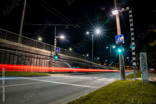 Long exposure photo of pedestrian walkway crossing and signs and markings on the road. Green traffic light and car in blurred motion driving on road. Riga, Latvia September 2024