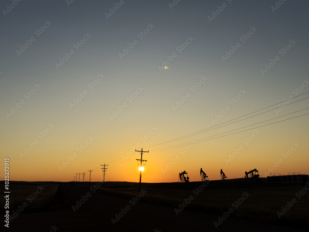 The sun rises behind transmission lines and pumpjacks in North Dakota