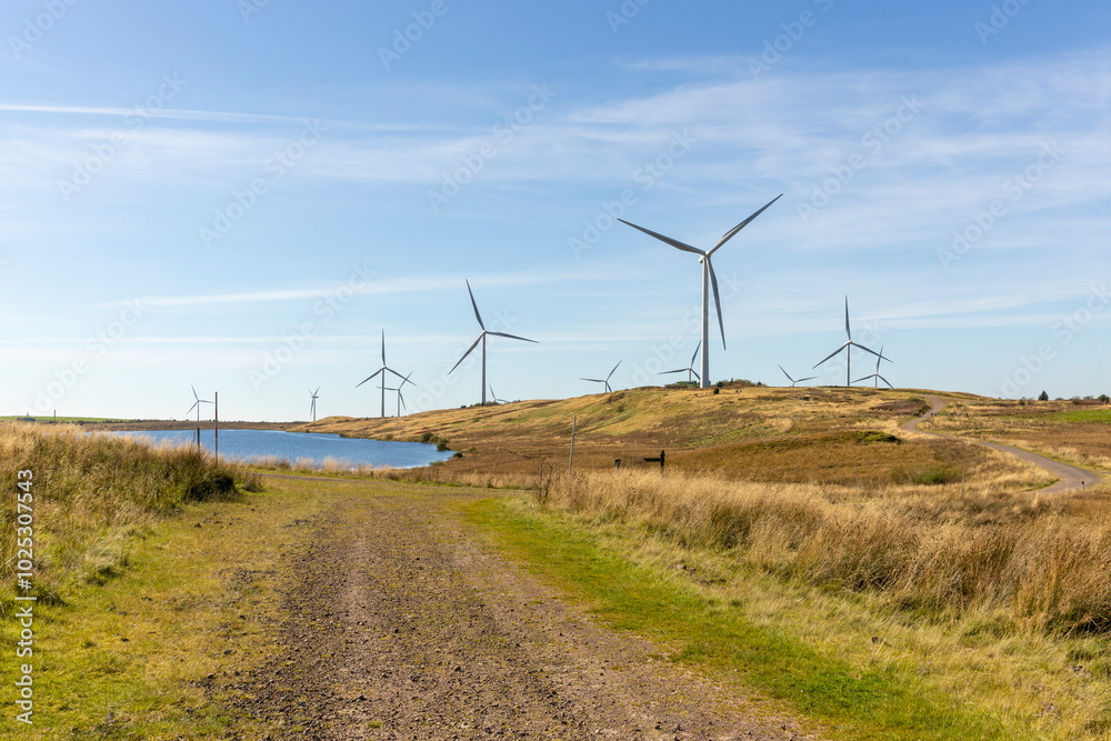 Gravel dirt track road leading to freshwater reservoir lake and wind farm turbines near on wild grassy moor land Gravel dirt track road leading to freshwater reservoir lake and wind farm turbines near on wild grassy moor land