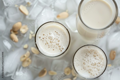 Vegan peanut milk being poured into three glasses with ice and scattered peanuts around photo