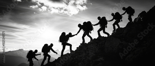 A group of people are climbing a mountain together. The image is in black and white and the people are silhouetted against the sky. Scene is one of teamwork