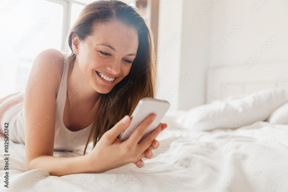 Smiling woman using smartphone in bed during the morning Smiling woman using smartphone in bed during the morning