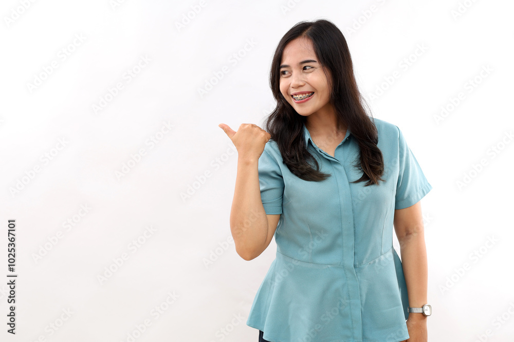 Young cheerful Asian female points away with thumb, happy face expression, demonstrates copy space for advertisement Young cheerful Asian female points away with thumb, happy face expression, demonstrates copy space for advertisement