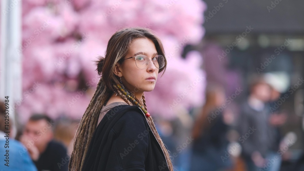 Fototapeta premium Portrait of a beautiful young woman with dreadlocks on a city street. A girl is sitting on the street in the food court area with a glass of coffee in her hand. She is getting ready to meet her