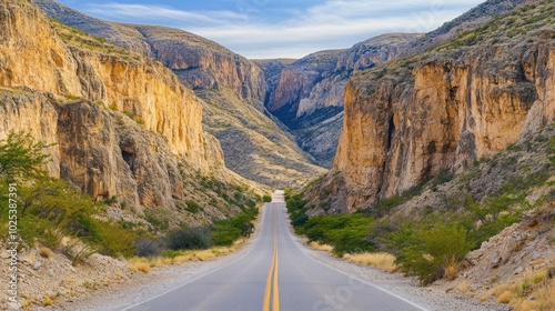 A scenic road winding through a canyon with towering rock formations on either side, with a blue sky and white clouds overhead.