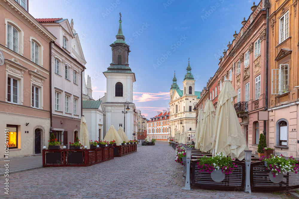 Obraz premium Street in the old town with historical buildings, colorful facades, church and street cafes in the early morning, Warsaw, Poland
